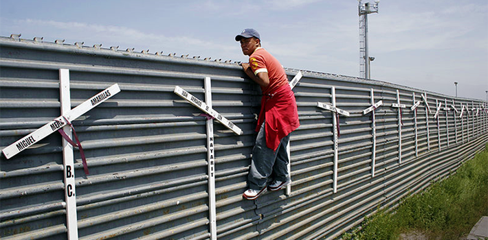 A migrant attempts to cross the US-Mexico border fence